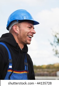 Happy Male Worker Outdoors In Blue Hardhat And Workwear