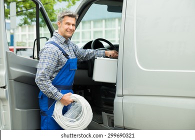 Happy Male Worker With Toolbox And Cable Coil Entering In Van