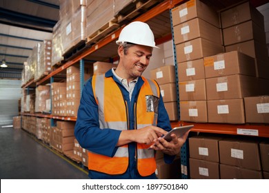 Happy male worker working in factory using digital tablet standing near the stack of cardboard boxes
