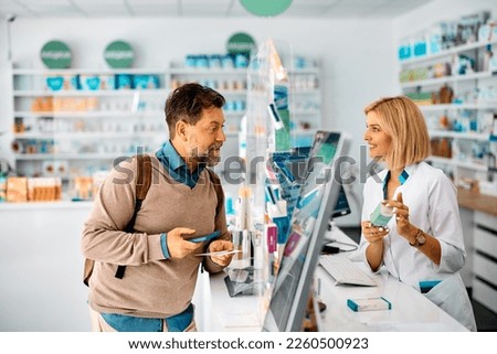 Happy man advising with his pharmacist while taking prescription medicine in a pharmacy.  