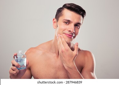 Happy Man Applying Lotion After Shave On Face Over Gray Background