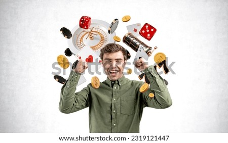 Happy man with arms raised, looking at the camera with casino jackpot and slot machine on grey concrete wall background. Concept of big win, luck and gambling