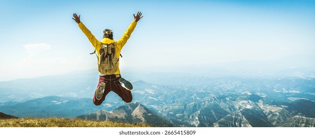 Happy man with backpack jumping on top of the mountain - Delightful hiker with arms up standing over the cliff - Sport and travel life style concept