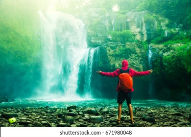 Happy Man Backpacker Enjoying Amazing Tropical Waterfall Raised Hands Travel Lifestyle And Success Concept Vacations Into The Wild Nature On Background Mountain