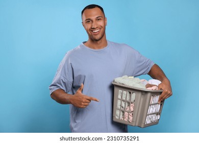 Happy man with basket full of laundry on light blue background - Shutterstock ID 2310735291