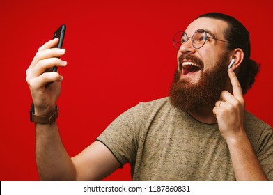 Happy Man With Beard Listening Music At Airpods Over Red Background