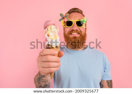 Happy man with beard and tattoos eats a big icecream