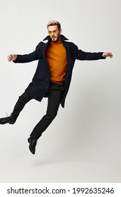 Happy Man In A Black Coat In Trousers And An Orange Sweater Jumped Up On A Light Background