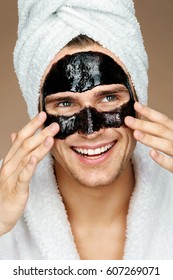 Happy Man With Black Mask On The Face. Photo Of Well Groomed Man Receiving Spa Treatments. Beauty & Skin Care Concept