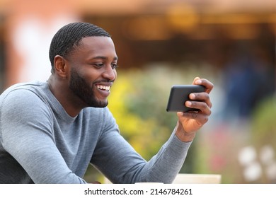 Happy Man With Black Skin Watching Media On Smart Phone In A Bar Terrace