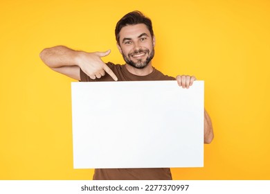 Happy man with blank banner isolated on studio background. Portrait of attractive man with empty blank poster. Man showing poster, pointing finger on signboard placard. Billboard or banner concept.