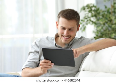 Happy Man Browsing In A Tablet Sitting On A Couch At Home