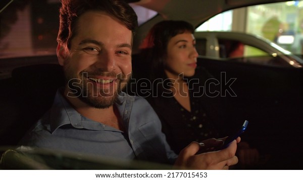 Happy man in\
car backseat at night after work portrait smiling holding\
smartphone device. Two people inside\
taxi