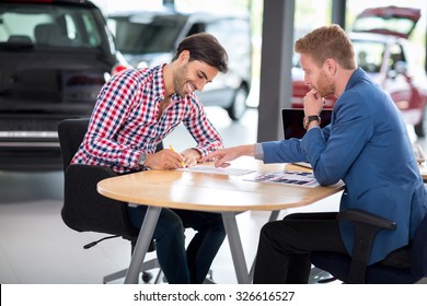 Happy man with car dealer buying a car signs the contract in car showroom