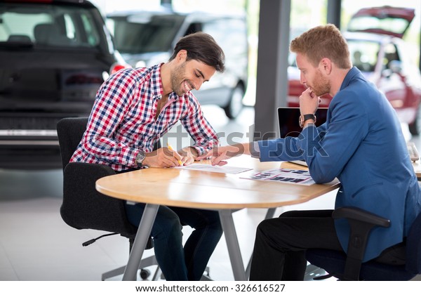 Happy man with car dealer buying a car signs the\
contract in car showroom