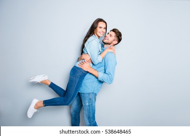 Happy man carrying his pretty wife on gray background.