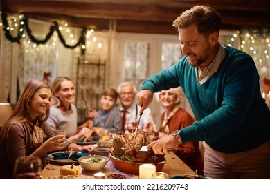 Happy Man Carving Turkey Meat During Thanksgiving Meal With His Extended Family.