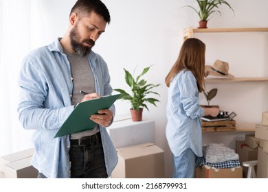 Happy man checking stuff in cardboard box before sent to transportation company and moving to new location apartment. couple checking things to do on clipboard - Powered by Shutterstock