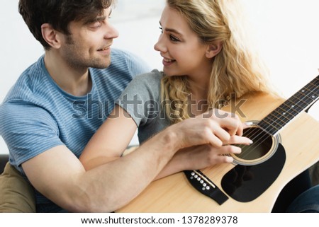 happy man and cheerful blonde woman holding hands of strings and looking at each other 