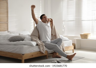 Happy man covered with beige plaid stretching in bedroom - Powered by Shutterstock