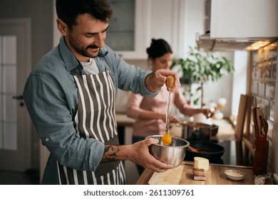 Happy man cracking an egg while preparing food in the kitchen.