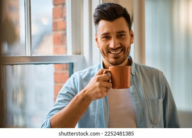 Happy man drinking coffee at home and looking at camera. - Powered by Shutterstock