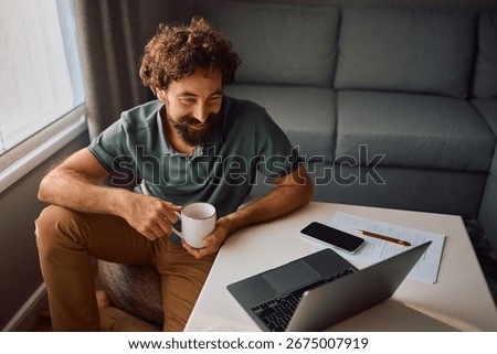 Happy man drinking coffee while using laptop at home.