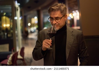 Happy Man Drinking Wine In Restaurant Holding Wine Glass, Smiling. 
Wine Tasting Expert. Portrait Of Mature Age, Middle Age, Mid Adult Man In 50s .