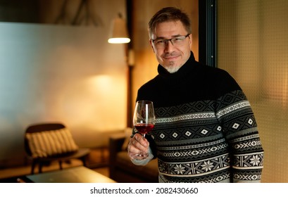 Happy Man Drinking Wine In Winter Holding Wine Glass, Smiling. Wine Tasting At Home. Portrait Of Mature Age, Middle Age, Mid Adult Man In 50s.