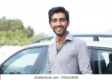 Happy man driver smiling standing by his new sport blue car isolated outside parking lot background. Handsome young man excited about his new vehicle. Positive face expression