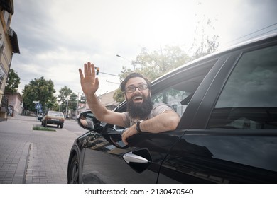 Happy Man Driving A Car And Waving Through The Opened Window, Saying Hello. City Positive People