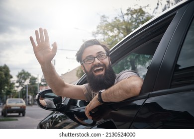 Happy Man Driving A Car And Waving Through The Opened Window, Saying Hello. City Positive People