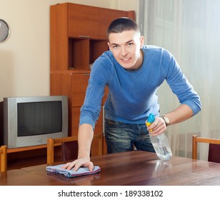 Happy man dusting table with detergent polish at home