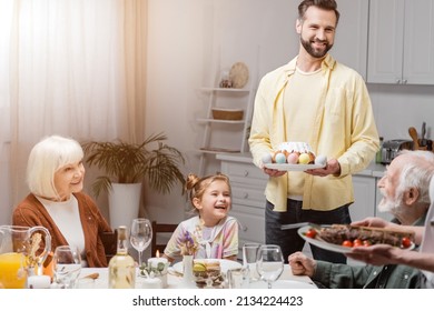 happy man with easter cake and painted eggs during easter dinner with family - Shutterstock ID 2134224423
