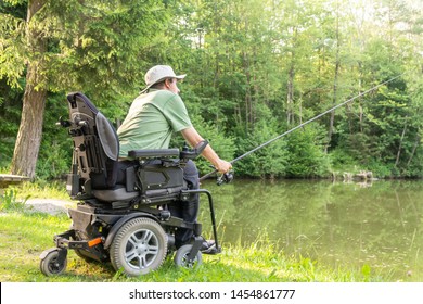 Happy man in a electric wheelchair throwing fishing pole at the beautiful pond in natue on a sunny day