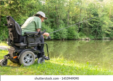 Happy man in a electric wheelchair waiting to catch a fish at the beautiful pond in natue on a sunny day