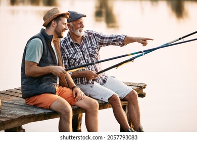 Happy Man Enjoying In Fresh Water Fishing With Is Father While Relaxing On A Pier. Father Is Pointing At Something In The Distance.