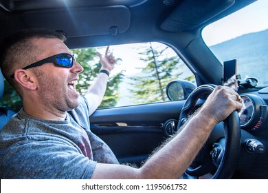 Happy Man Enjoying A Road Trip In His Car On A Sunny Day. Singing And Listening To Music In His Car On A Scenic Drive