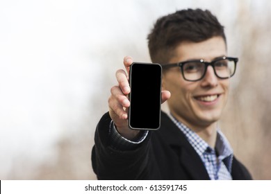 Happy man in expensive fashionable clothes and glasses for vision smiling close-up on city background with phone in hand.