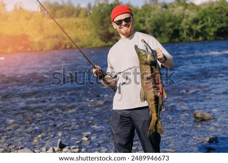 Happy man fisherman holding freshly caught big salmon fish from mountain river, concept fishing sport