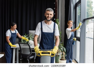 happy man with floor scrubber machine looking at camera near multiethnic women cleaning office - Shutterstock ID 2200925589