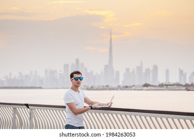 Happy man freelance programmer and junior developer writes code and thinks about a project in the paradise resort city of Dubai against the backdrop of the famous Burj Khalifa skyscraper
