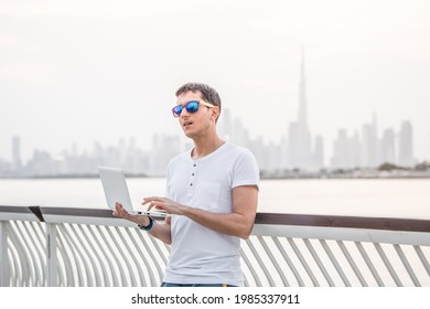 Happy man freelance programmer and junior developer writes code and thinks about a project in the paradise resort city of Dubai against the backdrop of the famous Burj Khalifa skyscraper