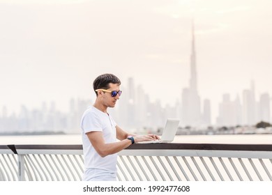 Happy man freelance programmer and junior developer writes code and thinks about a project in the paradise resort city of Dubai against the backdrop of numerous skyscrapers