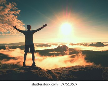 Happy man gesture of triumph with rams in air. Funny hiker on peak of sandstone rock in national park Saxony Switzerland watching to horizon