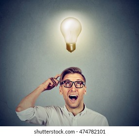 Happy man in glasses looking up at bright light idea bulb above head isolated on gray wall background - Shutterstock ID 474782101