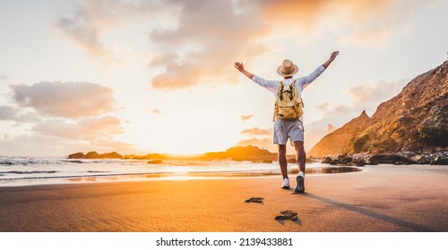 Happy man with hands up enjoying wellbeing and freedom at the beach - Male with backpack traveling in the nature with sunrise view - Healthy lifestyle, happiness and travel concept - Shutterstock ID 2139433881