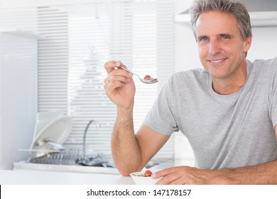 Happy Man Having Cereal For Breakfast In Kitchen At Home Smiling At Camera