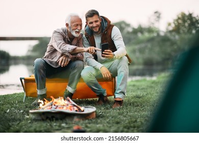 Happy man having fun while using mobile phone with his senior father by campfire at sunset.  - Powered by Shutterstock