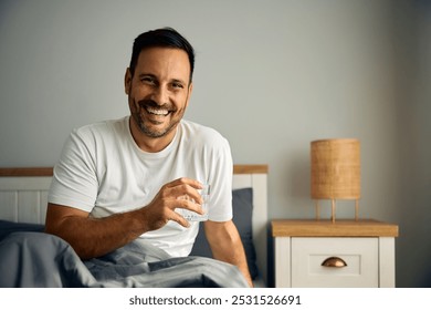 Happy man having a glass of water after waking up in bedroom and looking at camera.  - Powered by Shutterstock